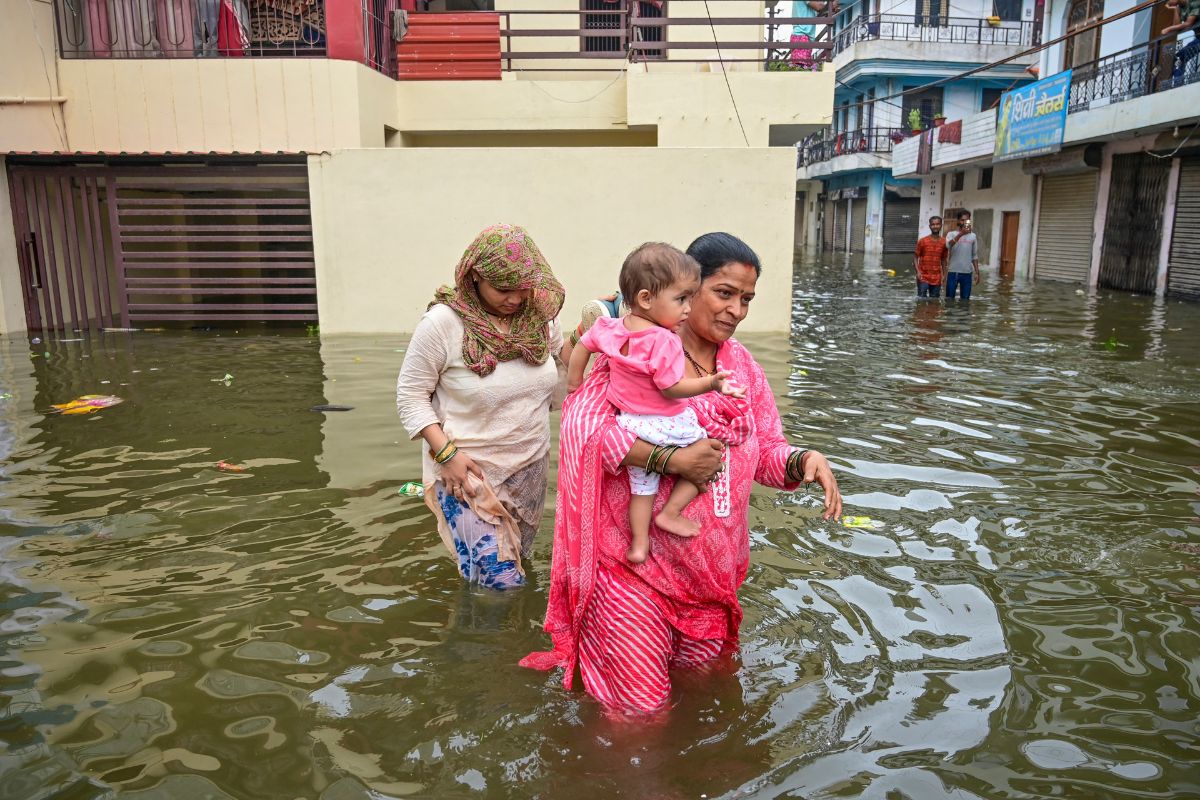 Flood: उत्तर प्रदेश में गंगा-यमुना उफान पर, 17 जिलों में बाढ़ का कहर, 400 से ज्यादा गांव जलमग्न 4 People-Wade-Through-Water